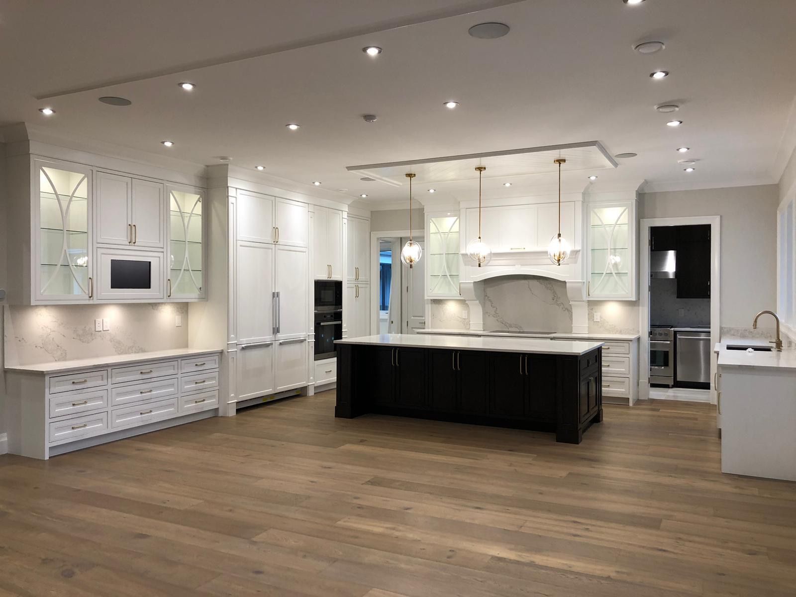 Large white kitchen with an espresso-stained island, brass pendant lights and glass-front display cabinets